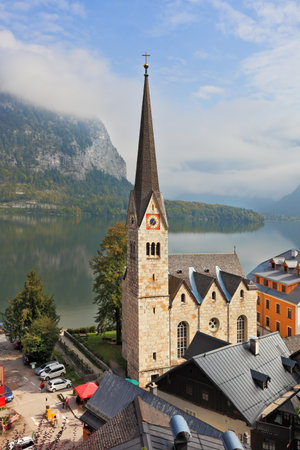 Slender belfry and Lutheran church on the shore of Lake Hallstatt  On the opposite shore of the lake - the beautiful mountains overgrown with forests  The most picturesque small town in Austria - Hallstattのeditorial素材