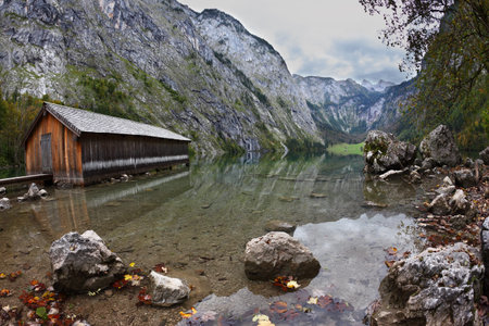 Cloudy day at Lake Koenigssee. Boathouse connected to the coast wooden decking. Clouds and mountains reflected in the waterのeditorial素材