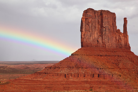 Navajo Reservation in the US. Red Desert and rocks - \"mitts\" sandstone. Huge rainbow crosses the cloudy skyの写真素材
