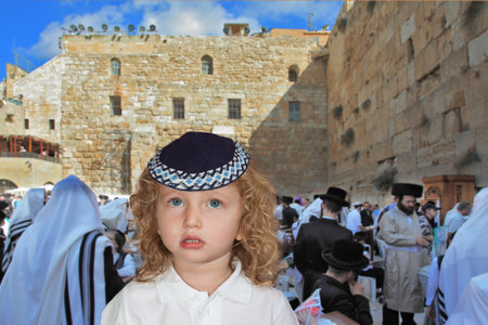 The lovely little boy with long light curls and blue eyes in a knitted skullcap. It costs at the main Jewish shrine - the Western wall of the Temple. Jewish holiday of Sukkotのeditorial素材