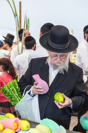JERUSALEM, ISRAEL - OKTOBER 8, 2014: Traditional market before the holiday of Sukkot. Orthodox Jew with a white beard in a black hat chooses citrusのeditorial素材