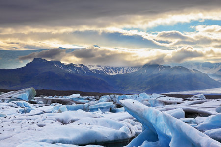 Blue and turquoise icebergs and cirrus clouds are reflected in the Bay JÃ¶kulsÃ¡rlÃ³n in...
