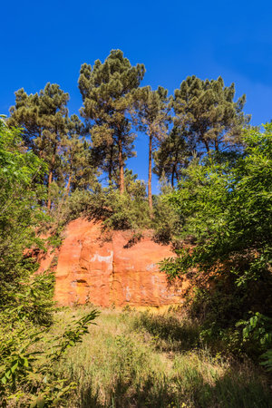 Unique red and orange hills in the province of Languedoc - Roussillon, France. Green trees create a...