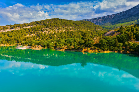 Mountain canyon Verdon in the French Alps. Smooth emerald green water of Lake Sainte-Croix-du-Verdon reflects the sky and wooded shoreの写真素材