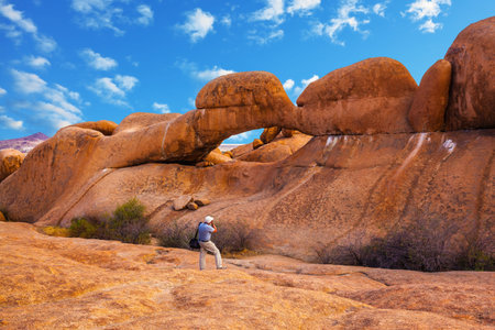 Nature reserve Spitzkoppe in Namibia. Picturesque stone arches are painted by iron oxides in red-orange color. Photographer enthusiastically takes the magical landscapeの写真素材