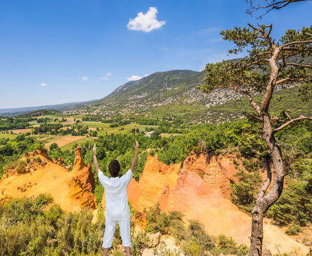 The elderly woman performs yoga in special form. Orange and red picturesque hills in Roussillon