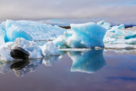 Blue and emerald icebergs and ice floes are reflected in smooth water of the Gulf  in Iceland....