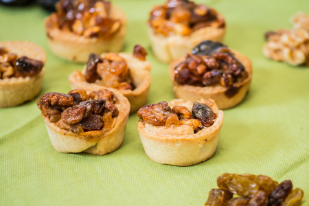 Professional baking. Background -green. Small portioned tartlet cakes with filling of nuts and dried fruitsの写真素材