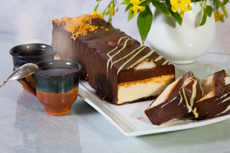 Delicious cheesecake with white and brown chocolate. The background is cup with hot tea and vase with flowers. Professional bakeryの写真素材