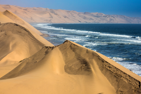 The concept of extreme and exotic tourism. Ocean surf with foamy waves. Jeep - safari through the huge sand dunes on the ocean shore. Atlantic coast of Walvis Bay, Namibia, south of Africaの写真素材