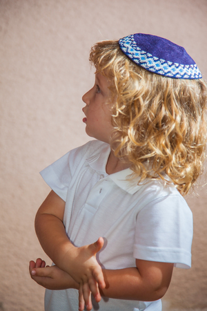 The charming little boy with long blond curls and blue eyes in the Jewish knitted yarmulke. Autumn holiday of Sukkotの写真素材