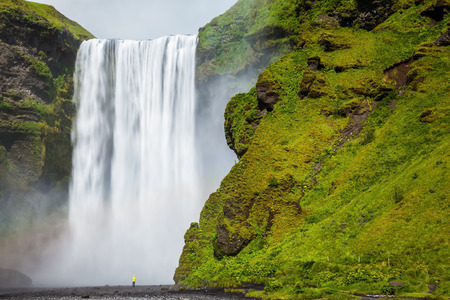 The most popular waterfall in Iceland - Skogafoss. Water rushes down with a crash, forming a cloud of mist. Picturesque huge rainbow appears in the water mistの写真素材