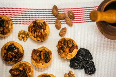 Magnificent portioned tartlet cakes with filling of candied nuts and dried fruits. Background wooden mortar with pestle. Professional bakingの写真素材