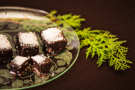 Professional baking. Portioned chocolate desserts sprinkled with coconut shavings. Beautiful translucent plate with patterns. Background brownの写真素材