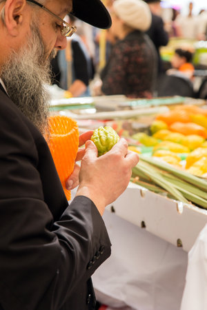 JERUSALEM, ISRAEL - OKTOBER 16, 2016: Traditional market before the holiday of Sukkot. Religious Jew in a black hat choose a ritual fruit - etrogのeditorial素材