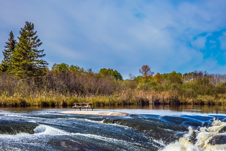The concept of travel "Around the World". Old Pinawa Dam Park. Magnificent rapids on smooth stones of the Winnipeg River. Yellowed autumn grass on banks of the riverの写真素材