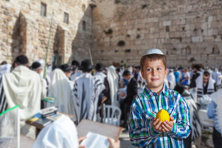 The greatest shrine of Judaism is the Western Wall of the Temple. Autumn Jewish holiday Sukkot. Beautiful Jewish boy in white skullcap, with etrogのeditorial素材