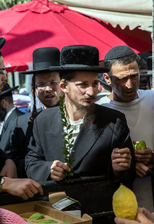  ERUSALEM, ISRAEL - OKTOBER 16, 2016: Traditional market before the holiday of Sukkot. Ancient Jewish holiday Sukkot. The buyer in a black hat chooses a citrus - etrogのeditorial素材