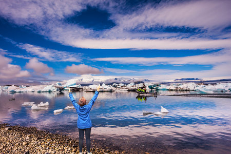 Morning in Drift ice of Ice Lagoon -Jokulsarlon. Elderly woman - tourist in a blue jacket watching...