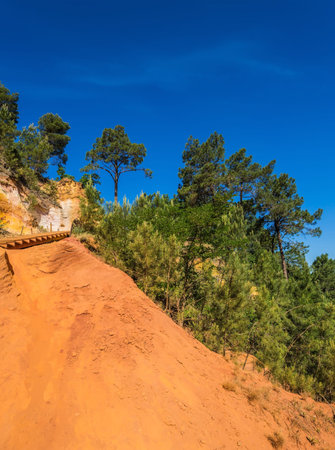 Unique red and orange hills in the province of Roussillon, France. Coniferous forests create a...