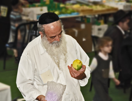 BNEY-BRAK, ISRAEL - SEPTEMBER 17, 2013: Big market on the eve of the Jewish holiday of Sukkot. The handsome elderly man with gray-haired beard and in skullcap chooses a citrusのeditorial素材