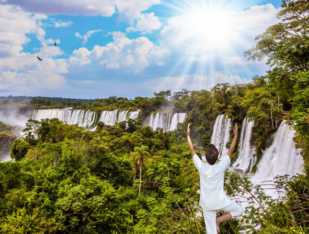 Elderly woman practicing yoga at the Iguazu Falls. The waterfalls from Iguazu Falls fall. The concept of extreme and ecological tourismの写真素材
