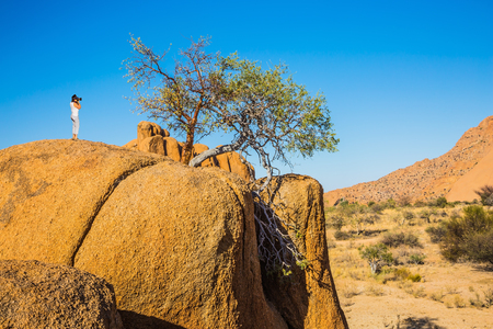 Slim woman on top of a huge stone photograph of a beautiful landscape. Picturesque stone in the Namib desert. Travel to Africa. The concept of active, extreme and photo-tourismの写真素材