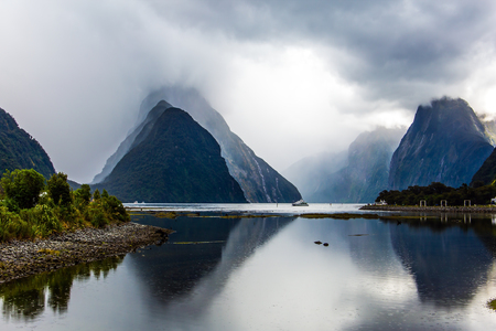 Land of hobbits and goblins. New Zealand. Mirror-smooth water of the Milford Sound fjord reflects mountains. Concept of exotic, ecological, active and photographic tourismの写真素材