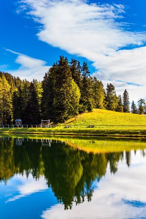 Alpe di Siusi is picturesque plateau in the Dolomites. The Val Gardena Valley. The pond reflects the sky and clouds. Beautiful day. The concept of walking, ecological and photo tourismの写真素材