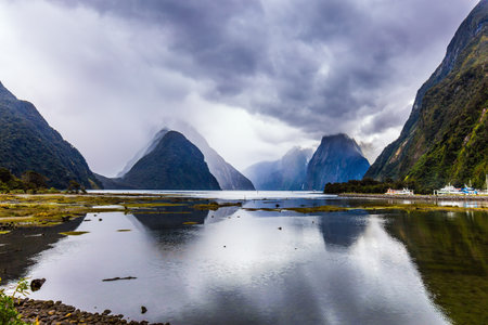Mirror-smooth water of the Milford Sound fjord reflects mountains. Storm clouds cover the sky. Magic country of fantastic heroes. New Zealand. Concept of exotic, active and photographic tourismのeditorial素材