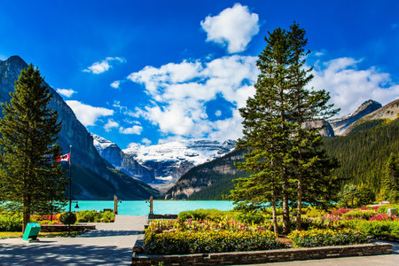 Sunny fine day. Glacial Lake Louise in Banff Park in Canada, Canadian Rockies. The lake embankment with green lawns and flower beds. The concept of ecological and photo tourismのeditorial素材