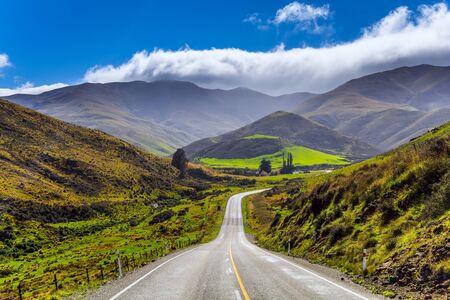 New Zealand Southern Alps. The road to the city of Cromwell among the mountains and meadows. The magic of New Zealand. Blue sky and clouds. The concept of ecological and photo tourismの写真素材