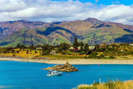 The most beautiful lake in New Zealand. Turquoise deep lake Wanaka with a fabulous island in the middle. On the lake sailing pleasure yacht. Magical journey to the ends of the earth. South Islandの写真素材