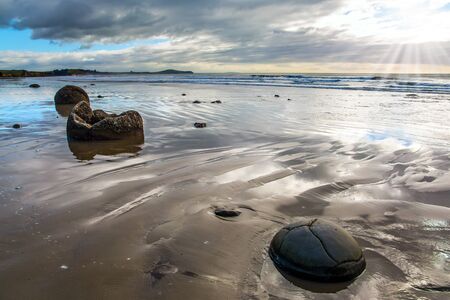  Moeraki's huge round boulders on a sandy beach. The Pacific ocean tide begins. New Zealand. The sun's rays are reflected in the ocean water. The concept of ecological, exotic and phototourismの写真素材