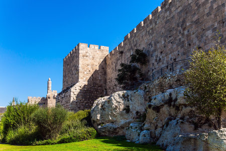 Hot summer sunset. The fortress wall of old Jerusalem. Ancient Citadel - Tower of David. Adorable green lawn growing under ancient walls. The concept of historical, pilgrim and photo tourismのeditorial素材