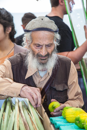 JERUSALEM, ISRAEL - OKTOBER 8, 2014: Traditional market before holiday of Sukkot.  Religious Jew with grey beard carefully examines ritual citrus - etrogのeditorial素材