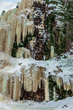 Multicolored ice streams on a steep cliff. Christmas in Lapland. Frozen waterfall in the winter forest. The concept of active, photo and eco-tourismの写真素材