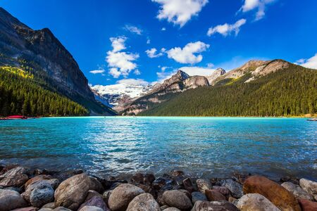 Glacial Lake Louise - the lake with azure water is surrounded by forests and mountains. Red canoes for tourists are moored to the coast. Rocky Mountains. The concept of active and photo tourismの写真素材