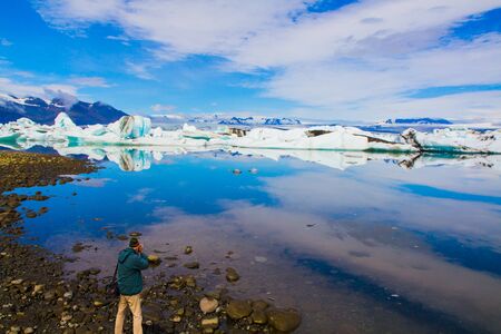 The man photographs the magnificent landscape. Iceland. White and blue icebergs and ice floes reflected in the lagoon Jokulsaurloun.The concept of extreme, northern and photo tourismの写真素材