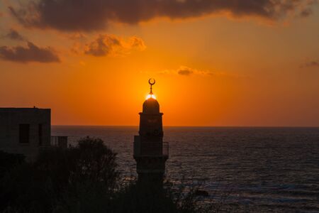 Round tower crowned with a crescent is a Muslim minaret. The setting sun plunges into the Mediterranean Sea. Old Yaffo, Tel Aviv. Concept active, informative and photo of tourismの写真素材