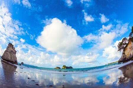 Mirror reflections of clouds in wet sand. Cathedral Cove on the North Island of New Zealand. Photo taken with fisheye lens.の写真素材