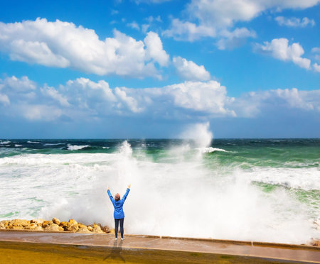 Woman in blue jacket admired by the power of the sea. Winter storm in the Mediterranean Sea. High...