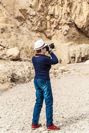 Slender elderly woman in jeans and a hat photographs the canyon. The coast of the famous Dead Sea. Stone canyon in the mountains of the Judean desert. Ecological, active and photo tourism conceptの写真素材