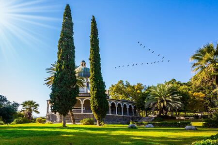 The bright rays of sunset illuminate the magnificent park. Flock of migratory birds flies. Church of the Beatitudes. High shore of Lake Tiberias. The concept of religious pilgrimage and photo tourismの写真素材