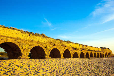 Magical sunset in Caesarea on the shores of the Mediterranean Sea. The ancient Roman aqueduct is lit by the setting sun. Summer in Israel.の写真素材