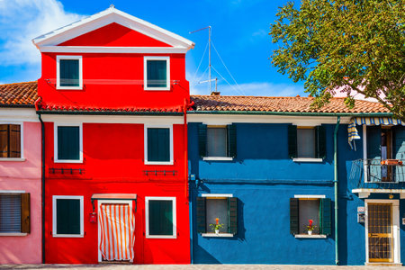 Burano is an island of colorful houses near Venice. Facade of a lovely multi-colored house. The balcony is decorated with flowers. Province of Veneto. The concept of historical and photo tourismのeditorial素材