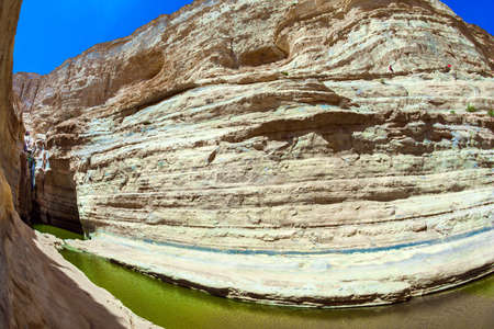 The canyon Ein Avdat is formed by the Qing River. Israel. The greenish mirror lake. Picturesque waterfall in the middle of the Negev desert. Photo taken with a fisheye lensの写真素材