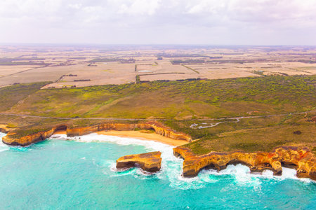 Helicopter flight over the scenic Pacific coastline. Cloudy day. Legendary cliffs "Twelve Apostles" in the snow-white foam of the ocean surf. Great Ocean Road. Bird's eye view. Australiaの写真素材