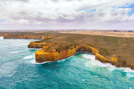 Helicopter flight over the scenic Pacific coastline. The fabulous journey to Australia. Cloudy cool summer day. Legendary cliffs "Twelve Apostles" in the snow-white foam of the ocean surf.の写真素材