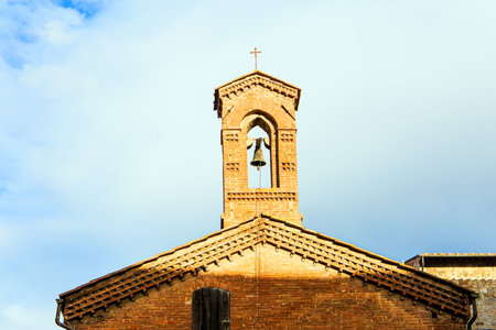 Bell tower with a bell topped with a cross. Winter trip to Tuscany. The old city center of Siena. Sunsetのeditorial素材